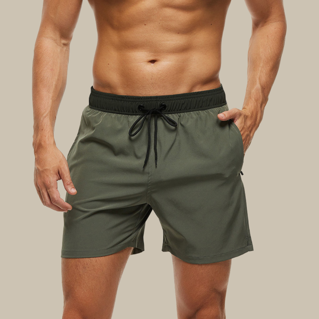 "Hurtigtørrende herrebadeshorts med lynlåslommer og elastisk pasform, set forfra, i blå polyesterstof."