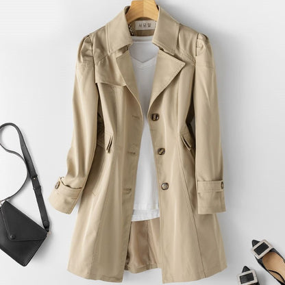 Kvindelig trenchcoat i beige med klassisk snit, knaplukning, letvægts og vandafvisende materiale. Set forfra mod baggrund.